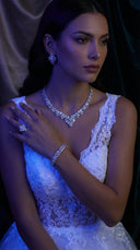 Woman wearing a white lace dress with jewelry, posing against a dark background