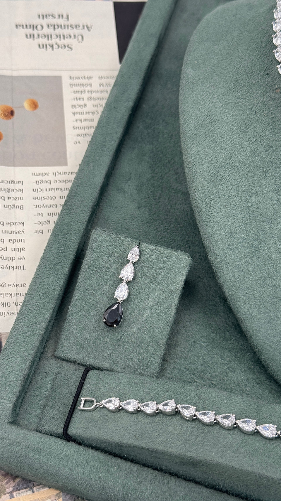 Black teardrop bridal earring with three clear pear cut stones beside a matching tennis bracelet