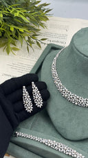 Pair of long pearl and zircon floral bridal earrings held over a black glove beside the matching necklace and bracelet