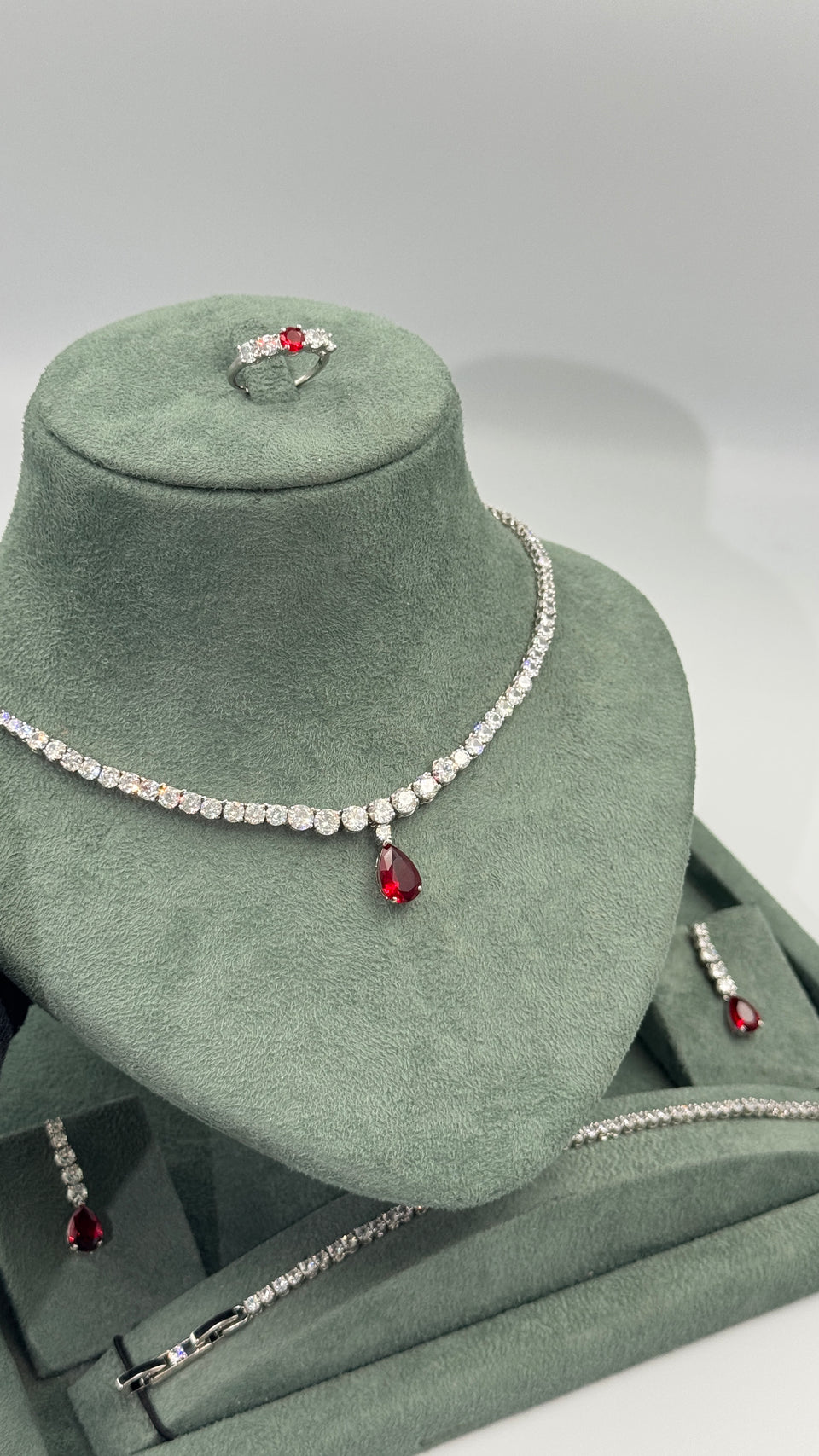 Ruby red teardrop bridal tennis jewelry set displayed with necklace earrings bracelet and adjustable ring