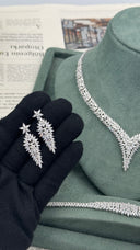 Pair of long marquise floral bridal earrings held over a black glove with the matching V necklace and bracelet behind