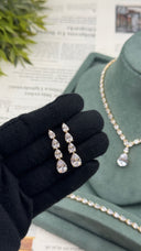 Gold-plated bridal drop earrings with four graduated pear-cut zircon stones, held beside the matching wedding set