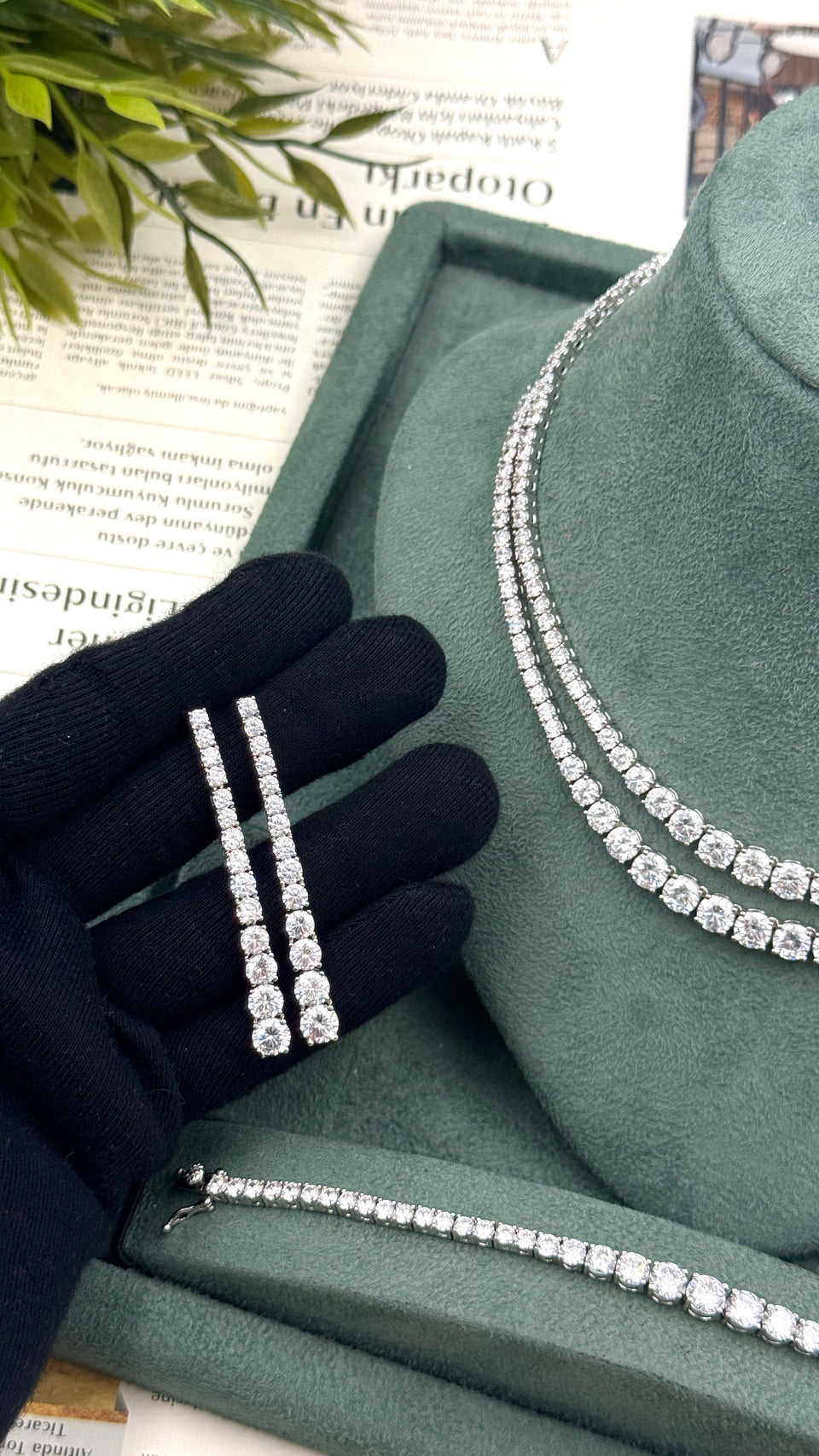 Pair of long graduated zircon bridal earrings held beside a matching double-row tennis necklace and bracelet