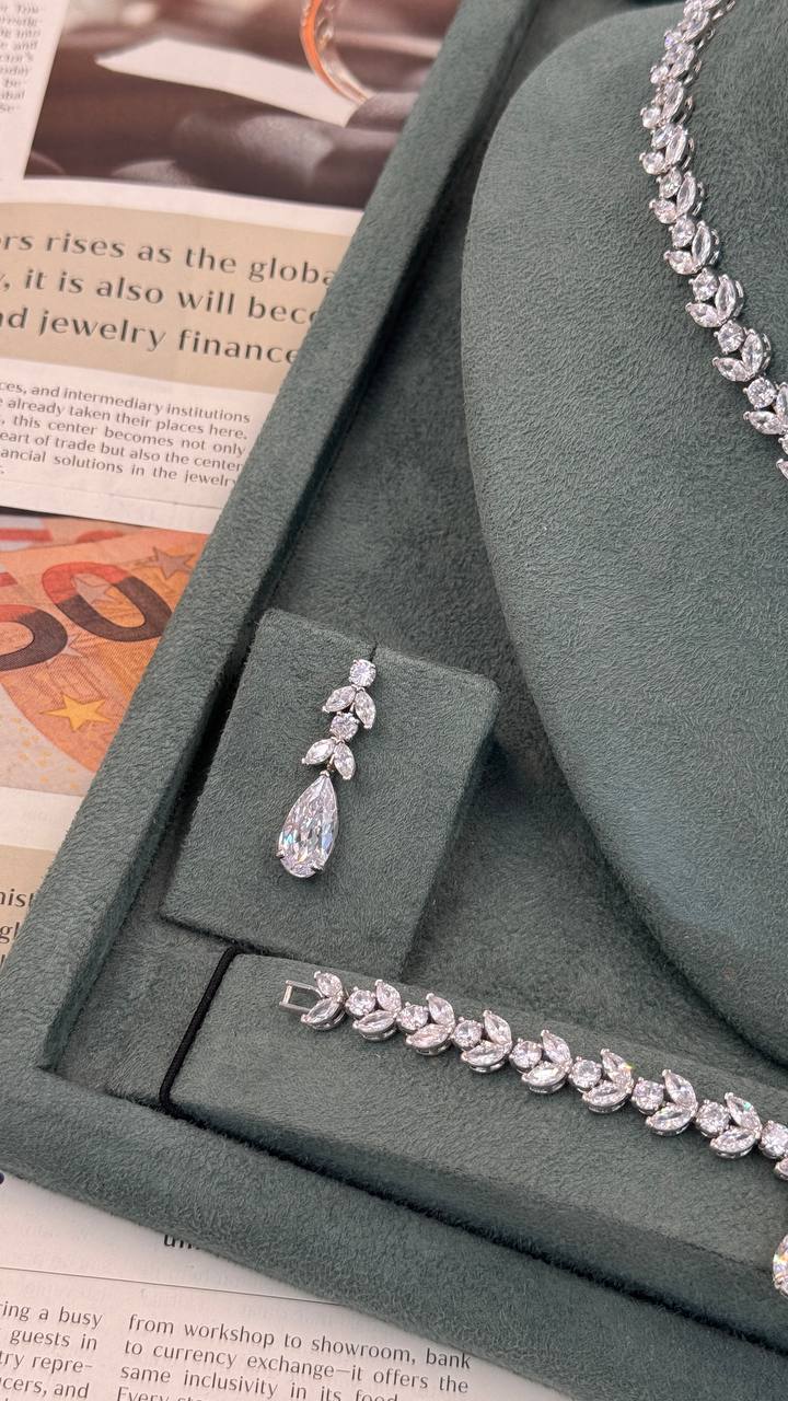 Pear-drop zircon bridal earring displayed beside a matching marquise leaf bracelet with floral centerpiece