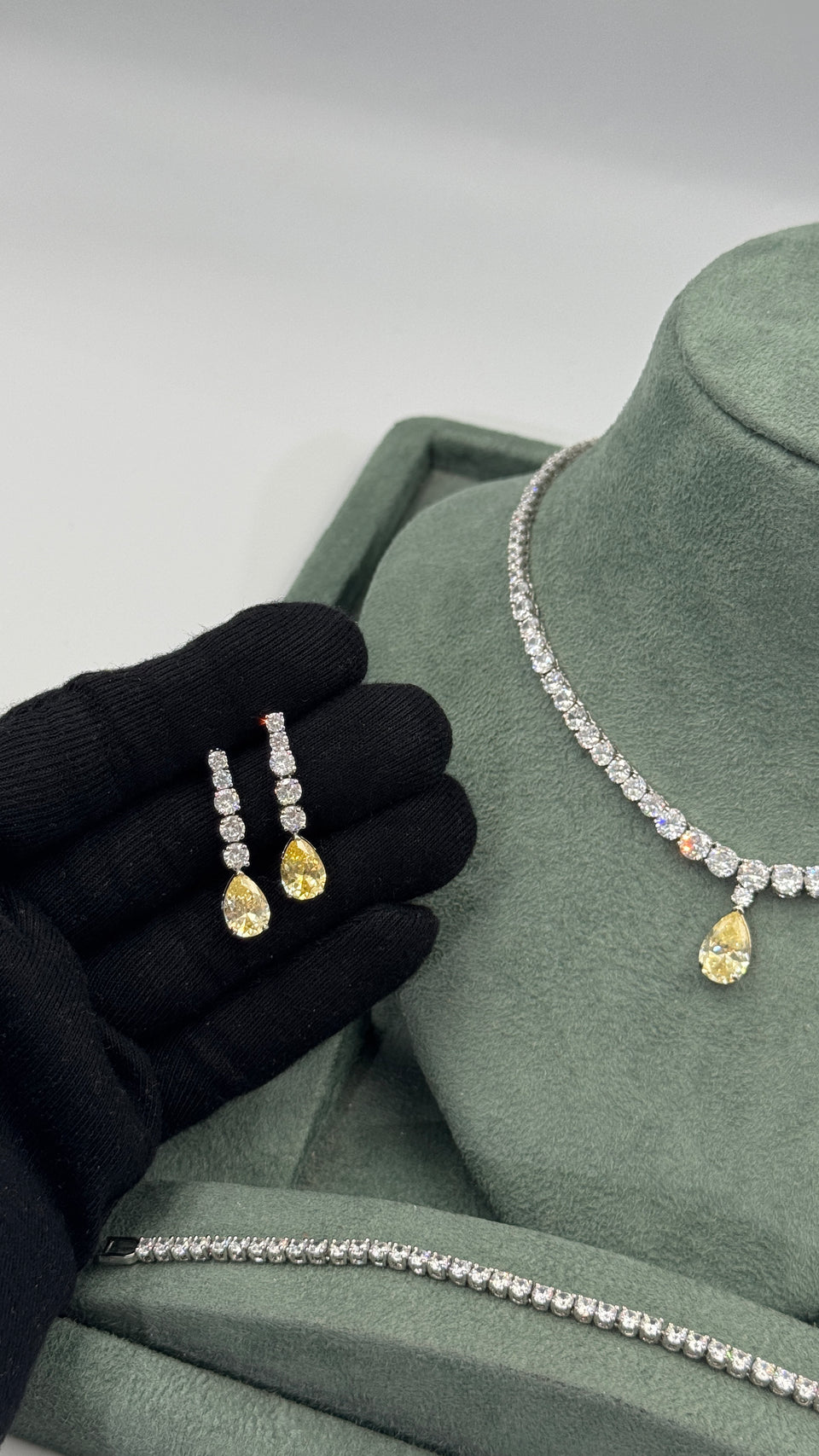Pair of clear round zircon bridal earrings with yellow pear-cut drops beside the matching tennis jewelry set