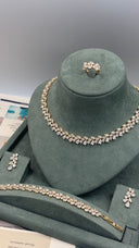 A gold-tone jewelry set displayed on a dark green velvet jewelry bust, including a necklace, bracelet, ring, and matching earrings with clear rhinestone-like stones.
