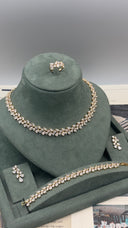 A gold-tone jewelry set with clear rhinestones displayed on a dark green velvet jewelry stand. The set includes a choker necklace, a matching ring, a bracelet, and two matching earrings.