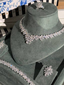 Silver jewelry set including necklace, ring, and earrings on a green velvet stand.