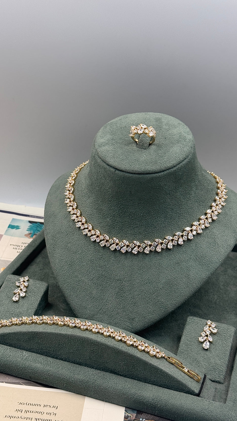 A gold-tone jewelry set displayed on a dark green velvet mannequin bust, including a necklace, matching bracelet, ring, and earrings, with a matching tray in front.