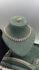 Gold-toned jewelry set displayed on a dark green velvet jewelry bust, including a necklace, ring, and bracelet with clear gemstones.