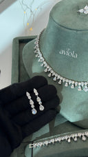 Pair of graduated pear cut bridal earrings held before a matching teardrop fringe necklace and bracelet