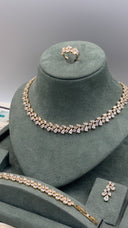 A jewelry set displayed on a dark green velvet mannequin bust, including a necklace, bracelet, ring, and matching pin. The jewelry features clear gemstones set in a yellow gold-tone metal.