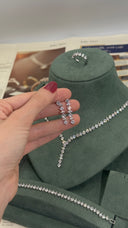 Silver jewelry set held by a hand with a green velvet display stand in the background