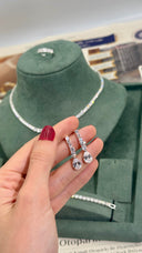 Hand holding a pair of silver earrings with a necklace on a green cushioned stand.
