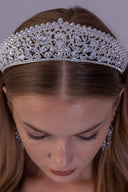 A close-up of a woman wearing an ornate silver rhinestone tiara headband, looking down. The headband is heavily embellished with clear crystals and silver-toned metal, styled on her brown hair.
